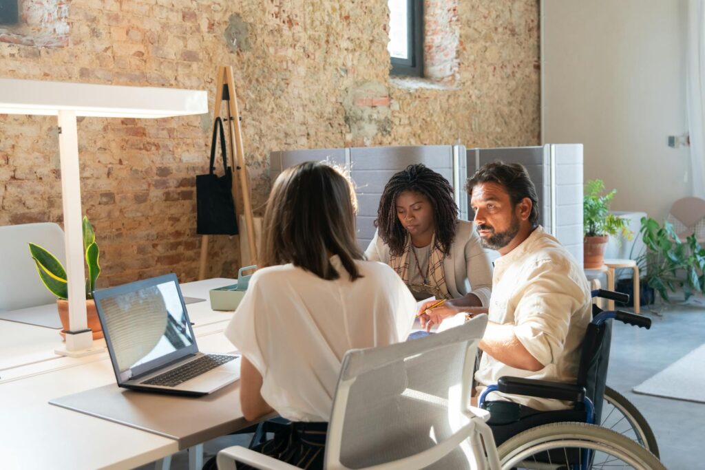 Consultorías Personas trabajando en al rededor de una mesa, una de ellas en silla de ruedas.